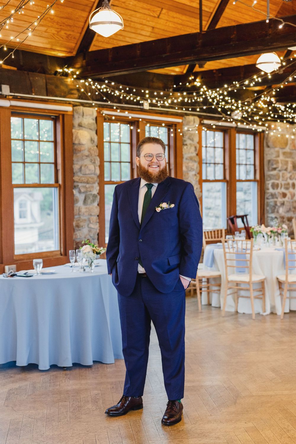 Wedding reception venue with rustic wooden ceiling, stone walls, white tablecloths and twinkling string lights.