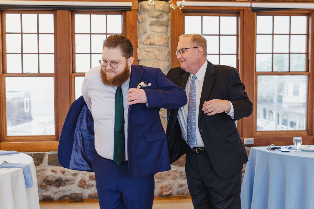 Wedding party in navy blue suits gather by windows in rustic venue during formal celebration.