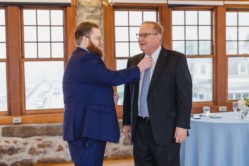 Two people in business attire converse in a bright room with large windows and stone walls.