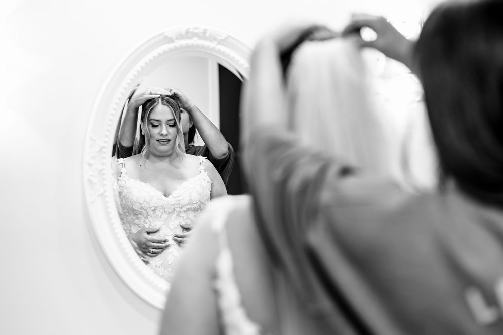 A delicate veil with lace details being adjusted in front of a mirror during wedding preparations.