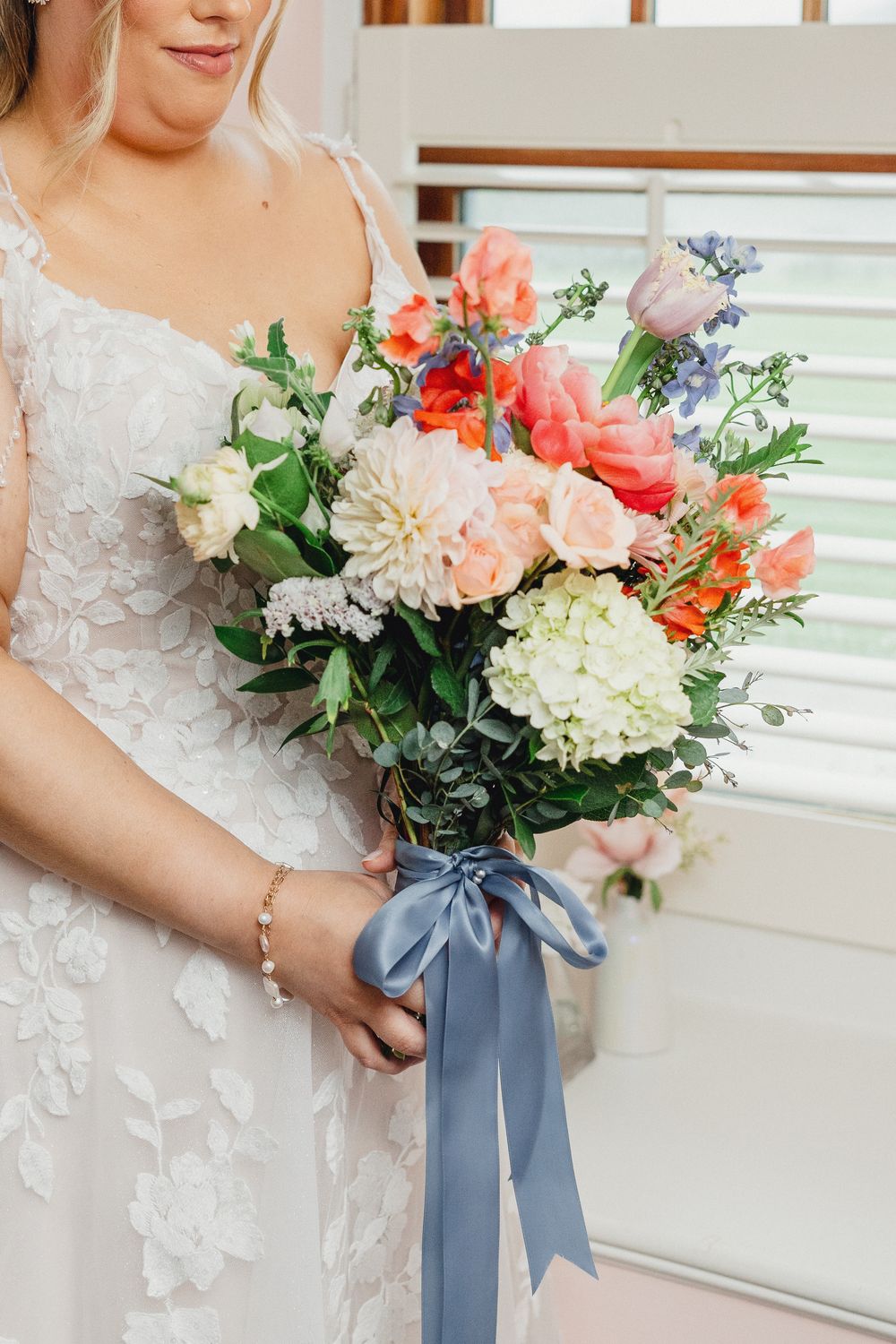 A bridal bouquet featuring coral and white flowers tied with a dusty blue satin ribbon.