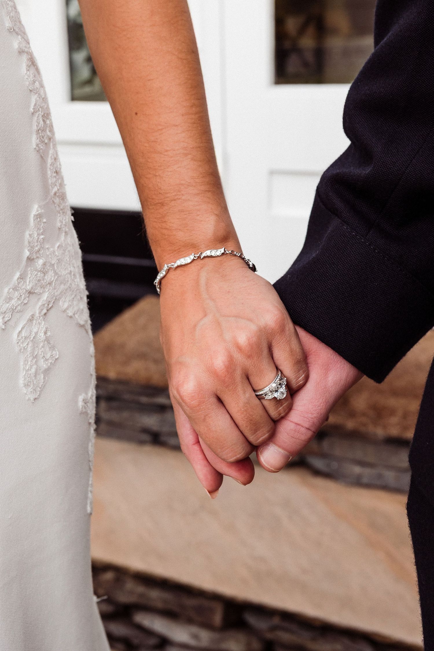 Close-up of newlyweds holding hands showing wedding rings and delicate bracelet details.