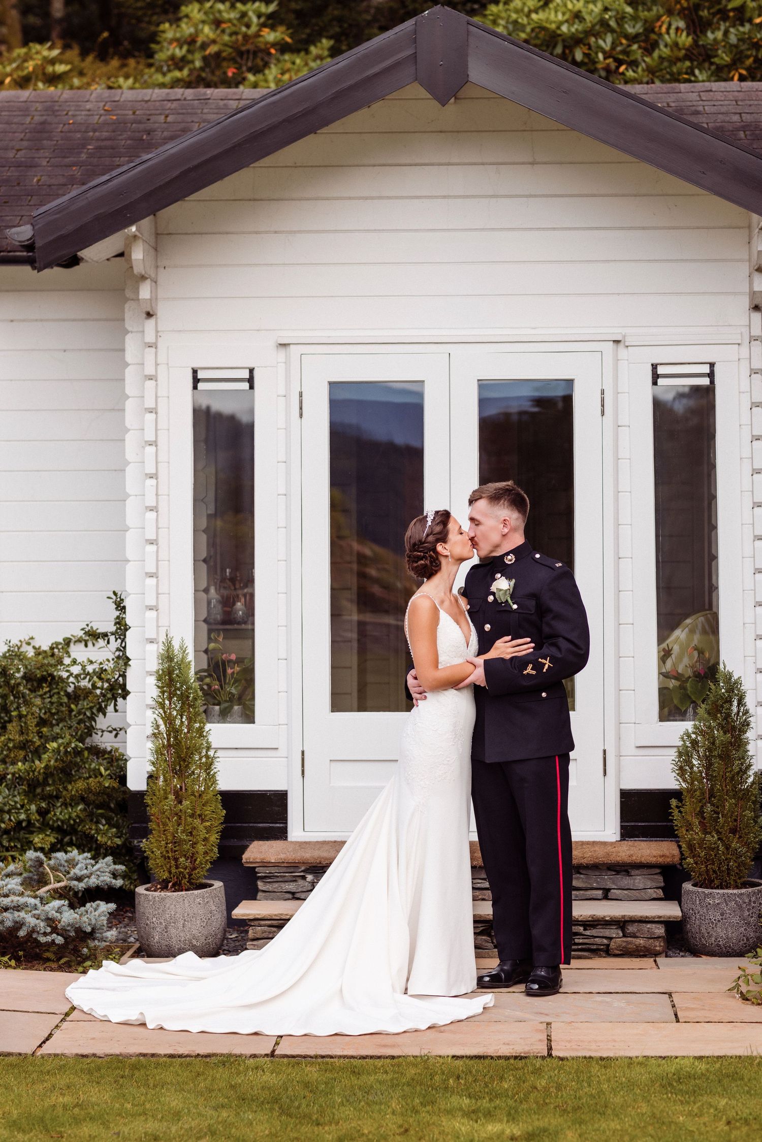 A couple shares a romantic moment outside a white cottage-style building with French doors.