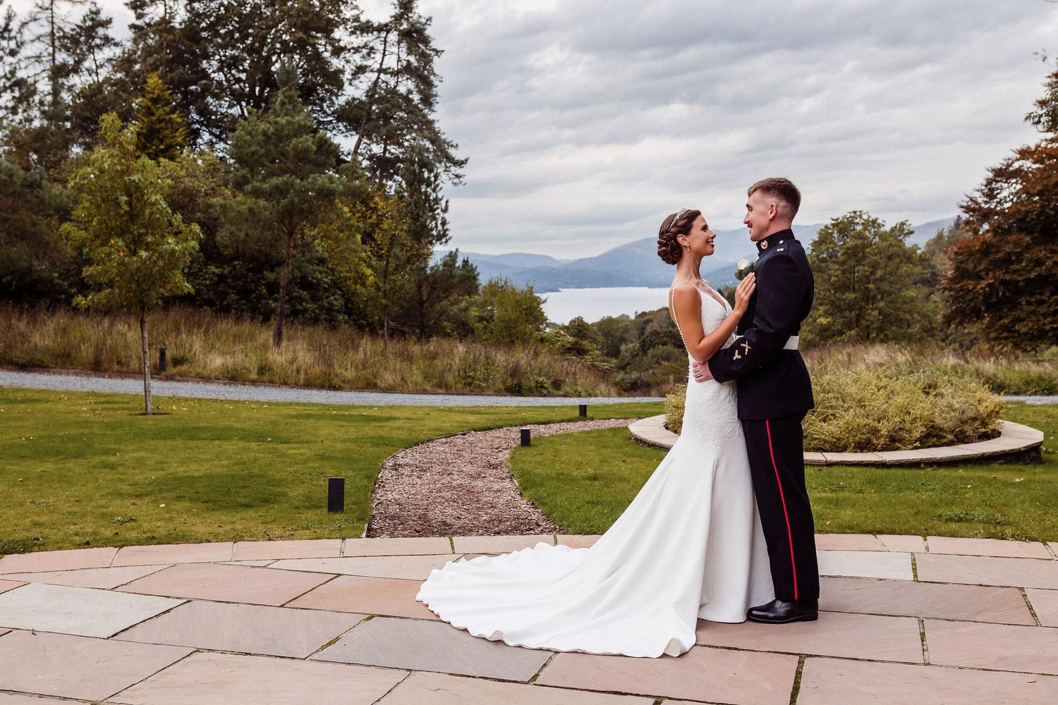 Couple embracing on stone patio with scenic mountain landscape and autumn trees in background.