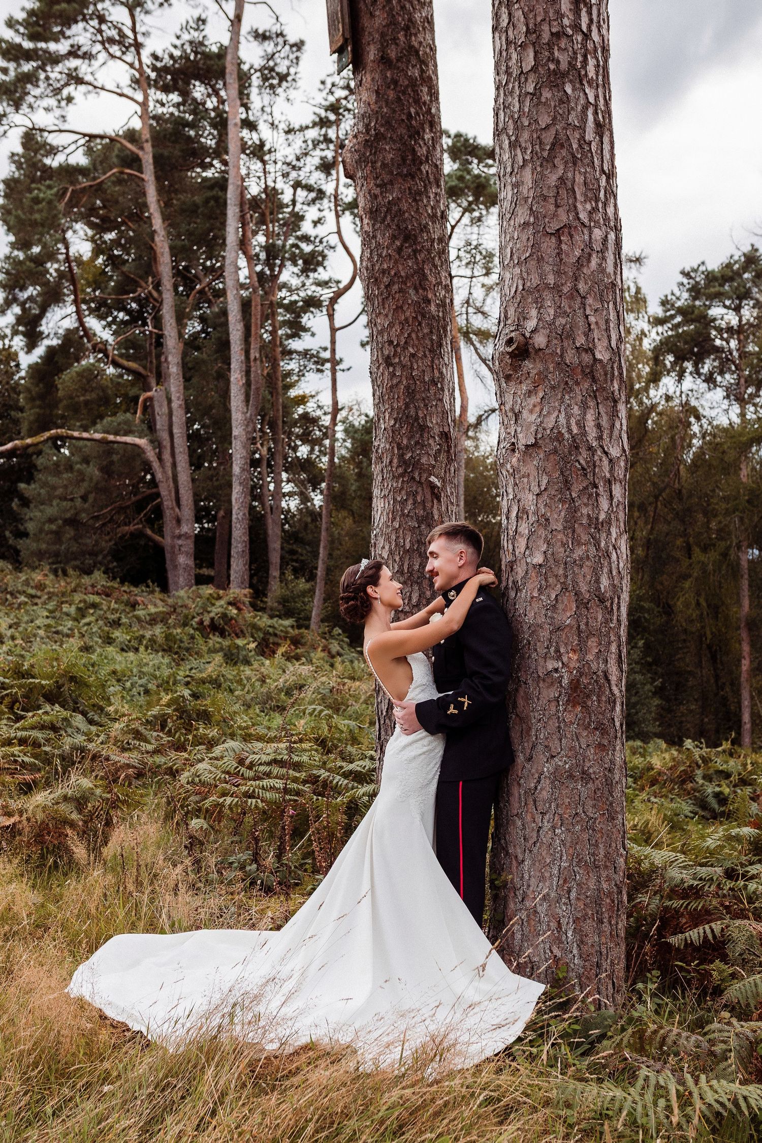 A couple embraces against tall pine trees in a romantic forest wedding photo.