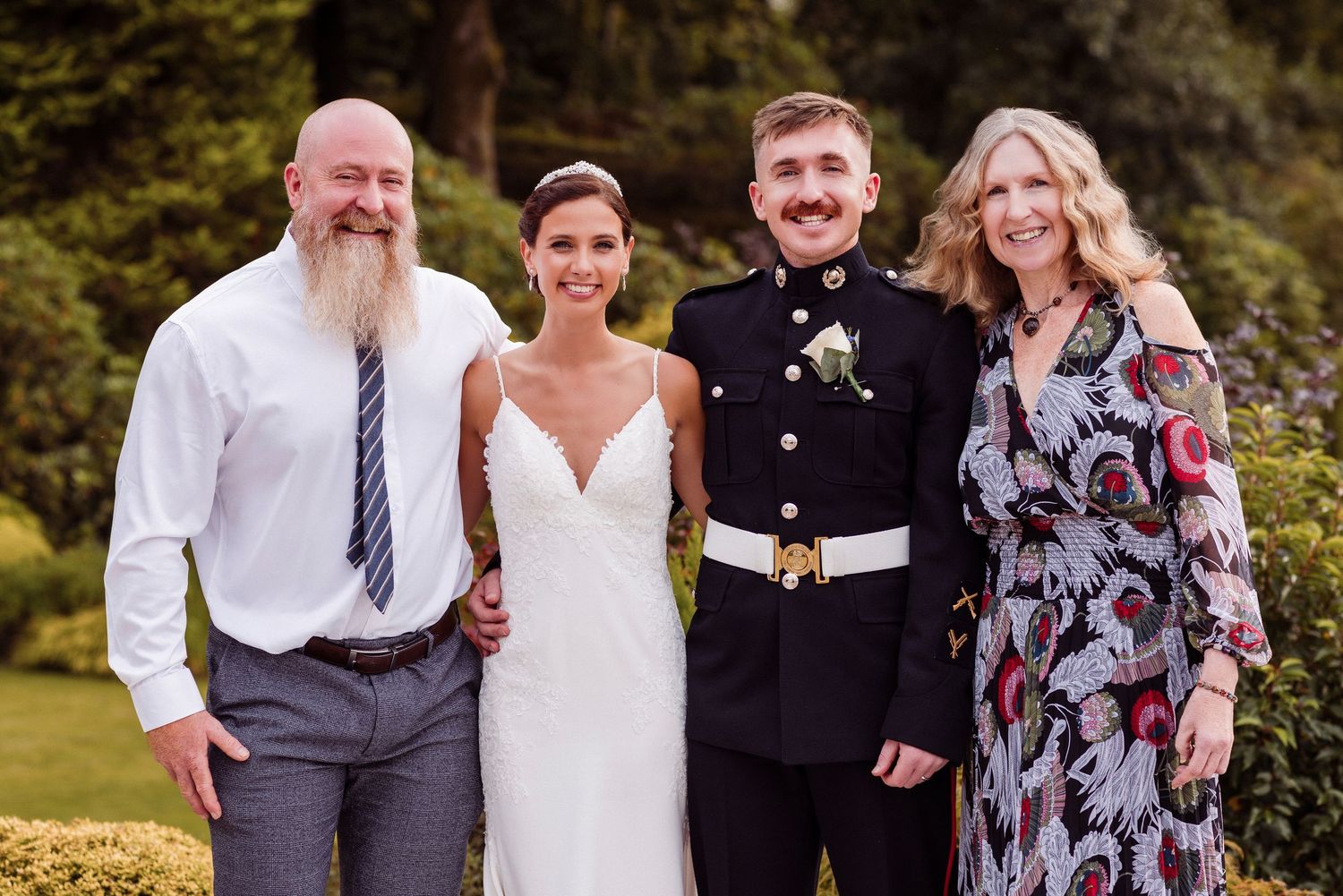 A wedding party poses together outdoors in formal attire on a sunny day.