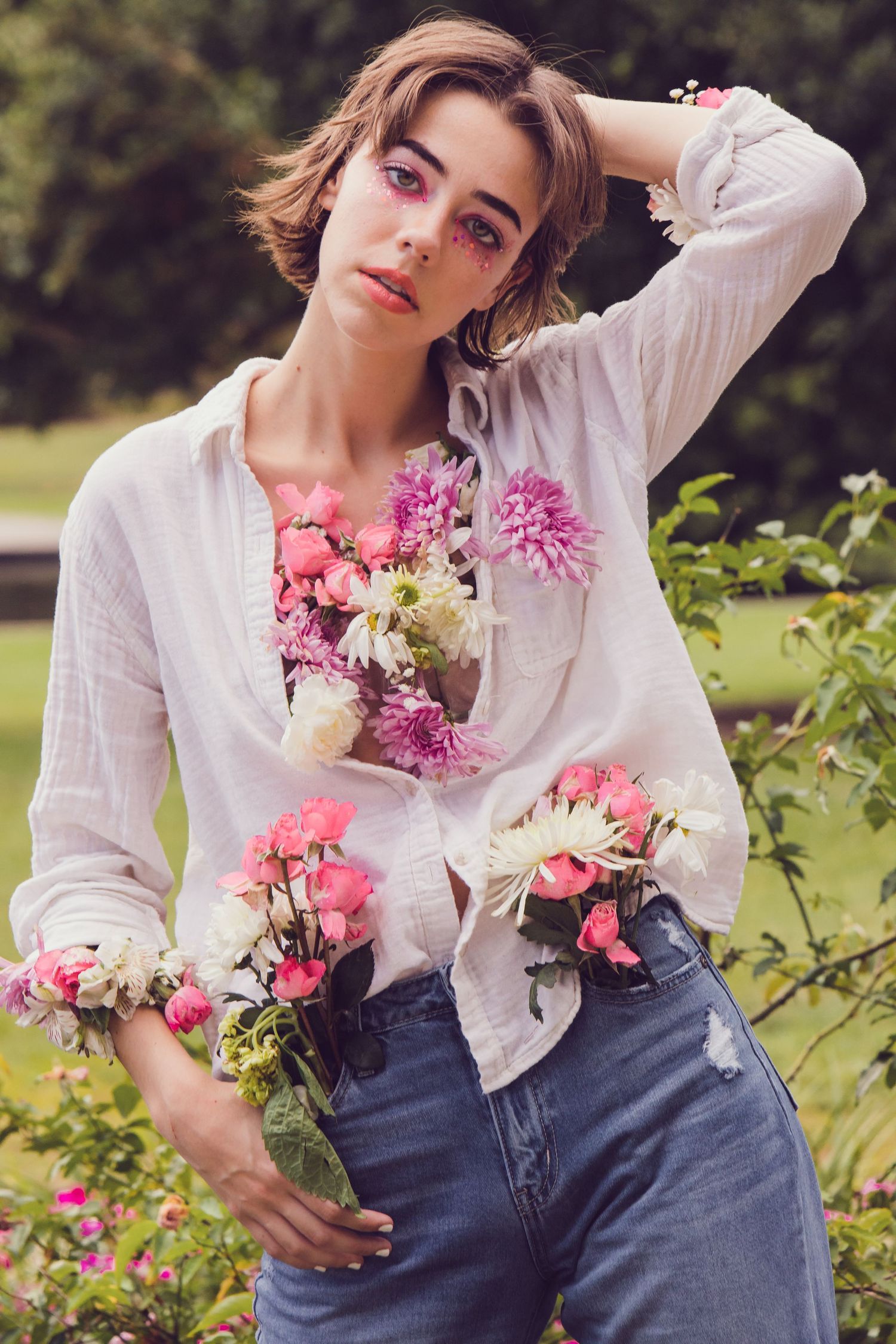 A fashion portrait in a garden setting with a white blouse, denim jeans, and pink flowers creating a romantic mood.