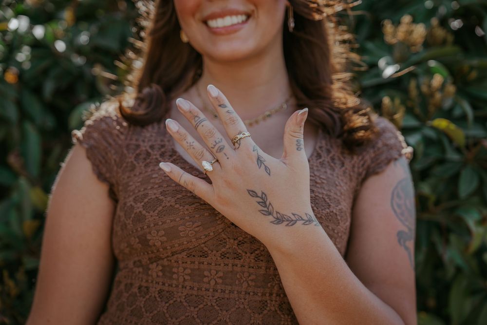 A person wearing a brown knit top shows off intricate henna designs on their hand against a green leafy background.