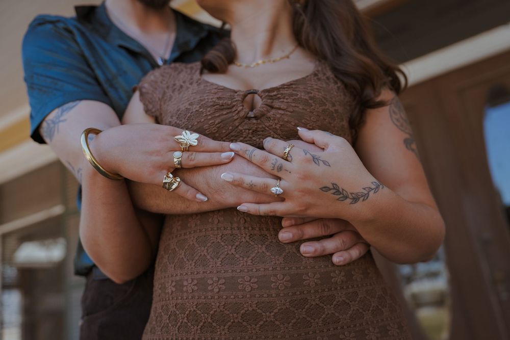 Close-up of hands with rings embracing a pregnant belly in a brown dress.