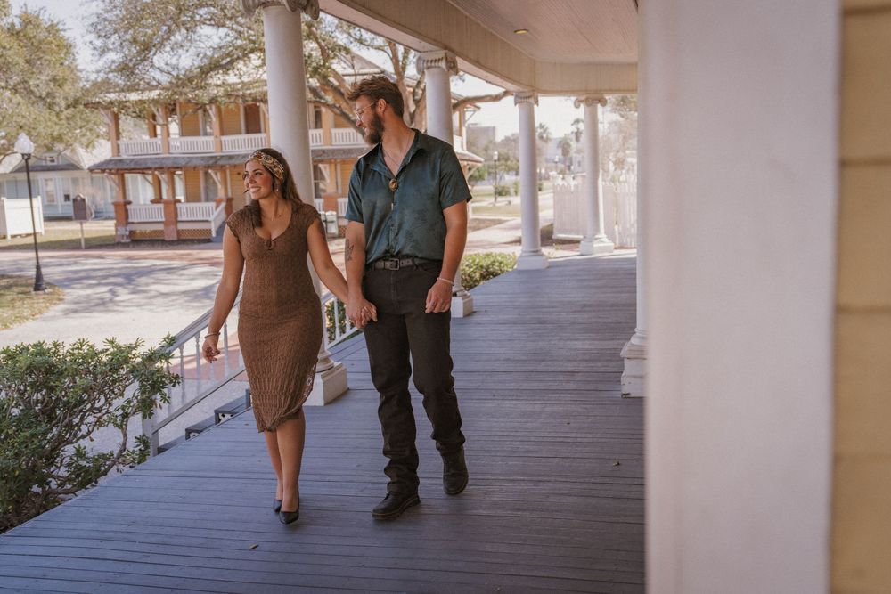 A couple walks together along a covered outdoor walkway on a sunny afternoon.