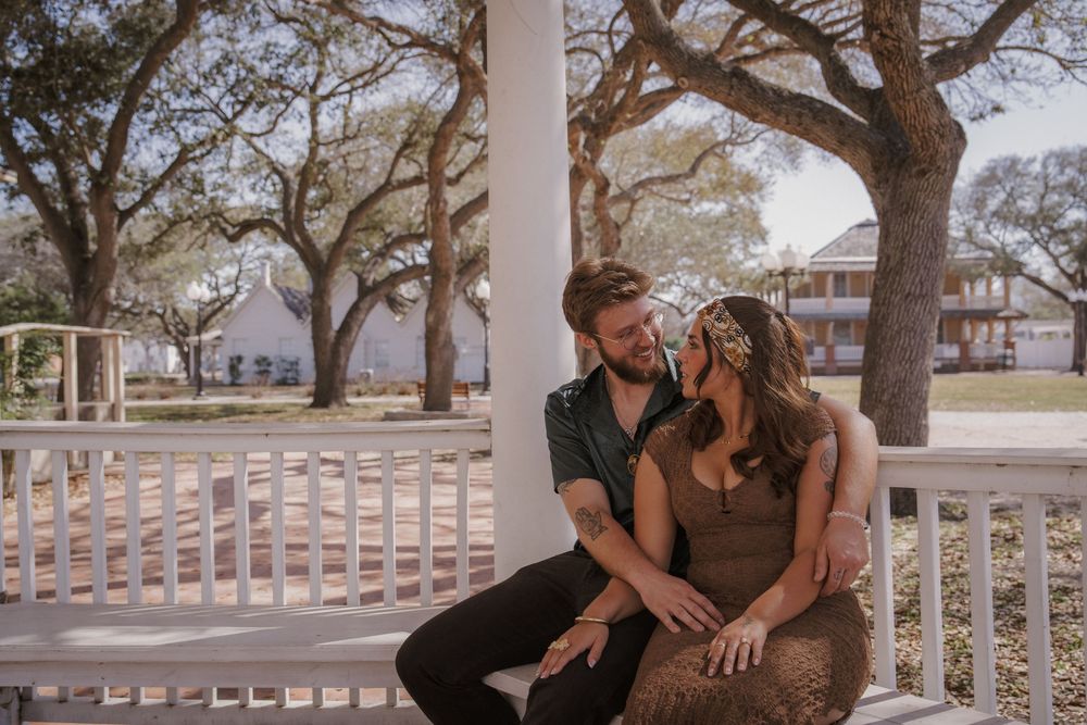 A couple shares intimate moments on a porch with white railings at sunset.
