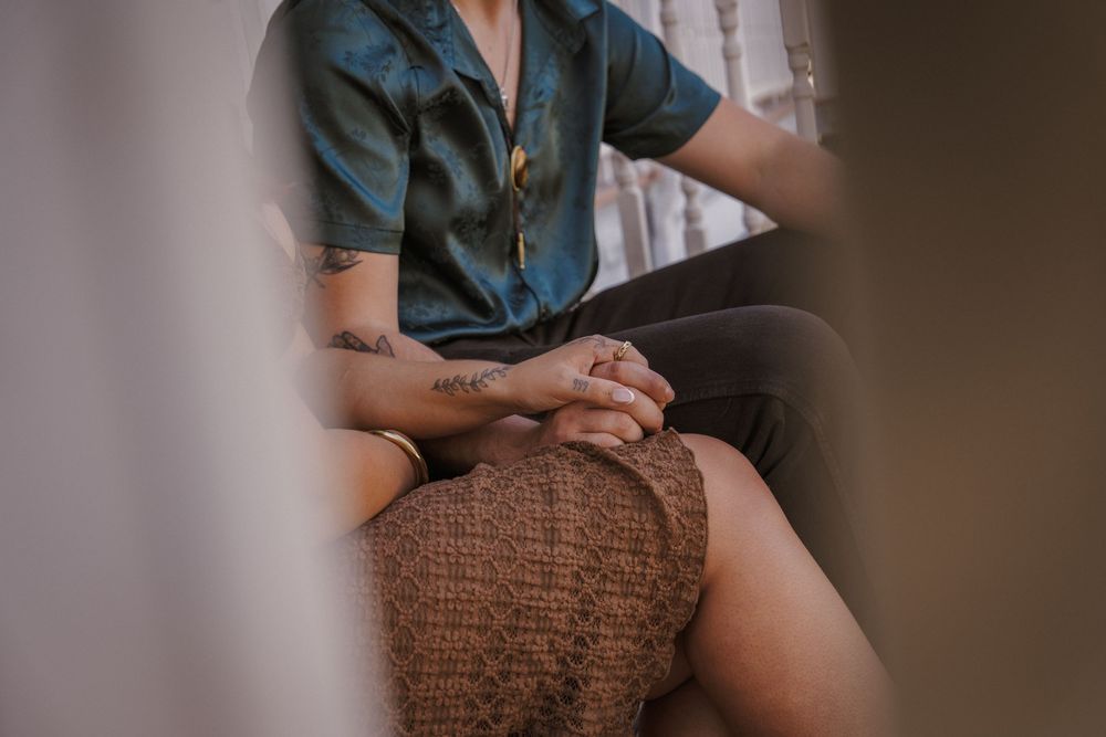 A person sits on a couch wearing denim shorts and a blue top while holding a brown knitted blanket.