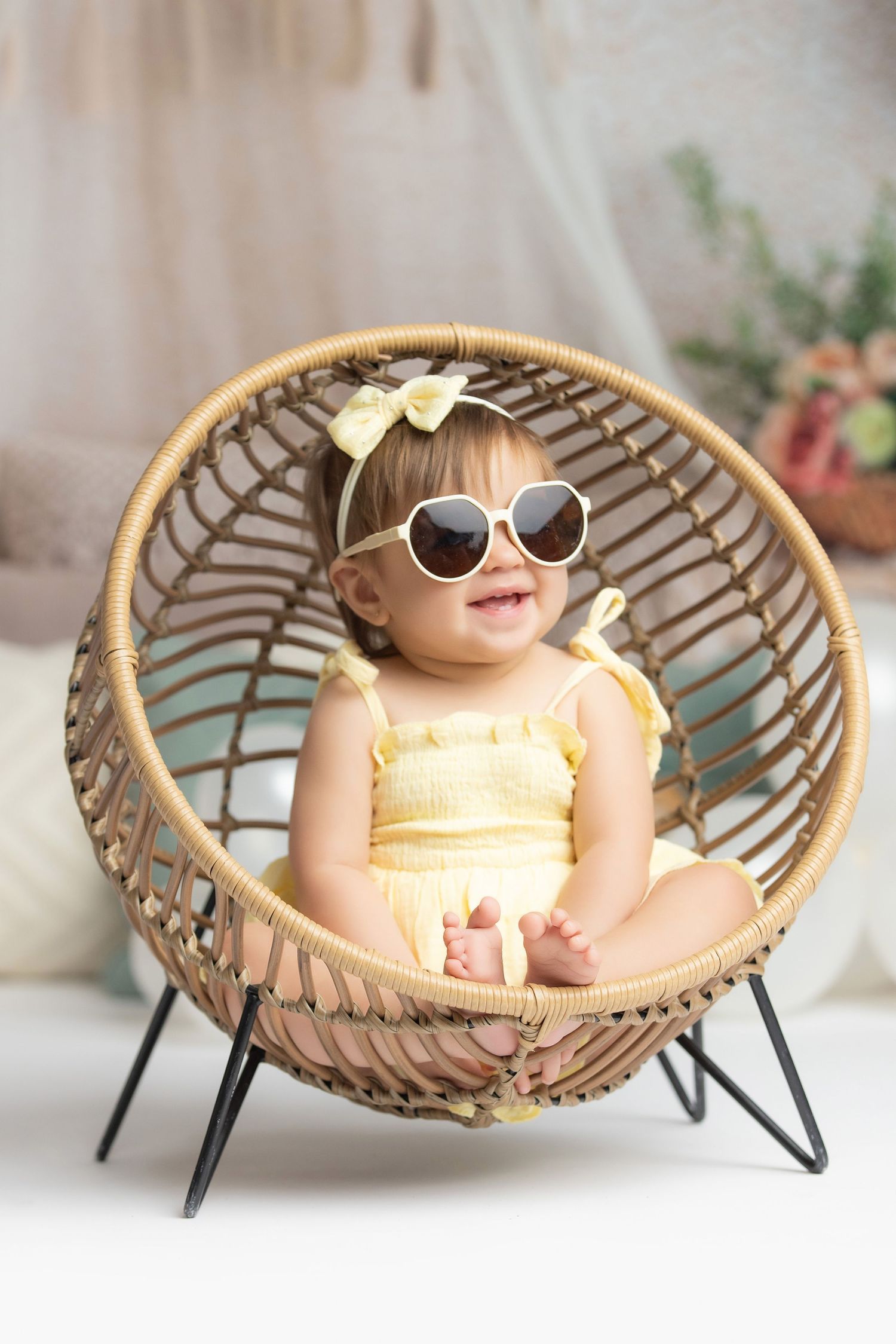 A small child wearing sunglasses lounges in a modern rattan papasan chair against a light background.