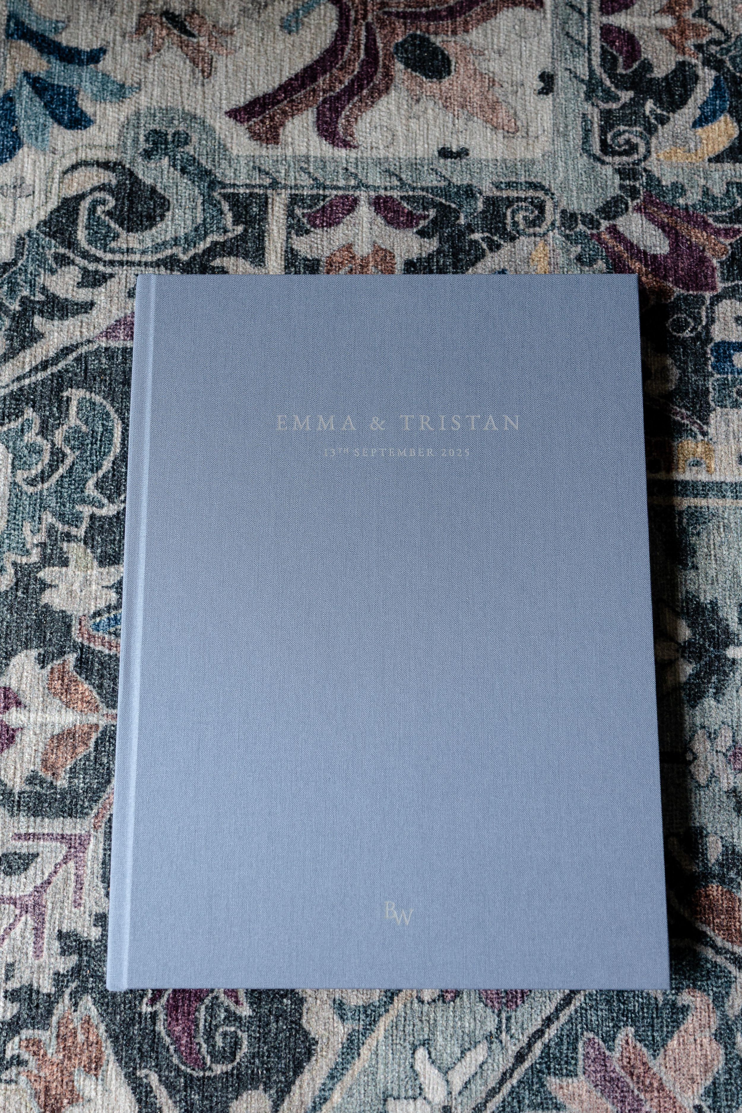 Three gray hardcover photo albums or books arranged on a decorative patterned surface.