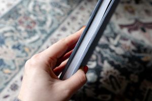 Hand with red nail polish holds a dark smartphone against a floral patterned rug background.