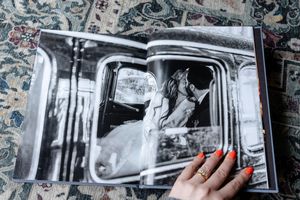A hand touches a black and white wedding photo in an album showing a bride sitting in a vintage car.