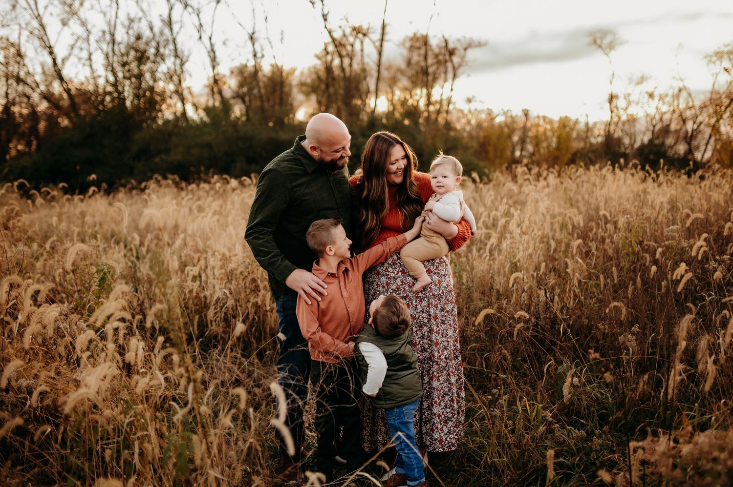 A family shares tender moments together in a golden sunlit field during sunset.