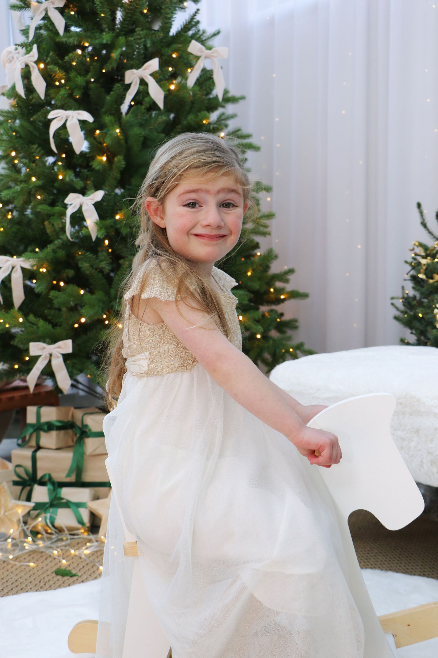A child in a white dress twirls and dances in front of a decorated Christmas tree with white bows and lights.