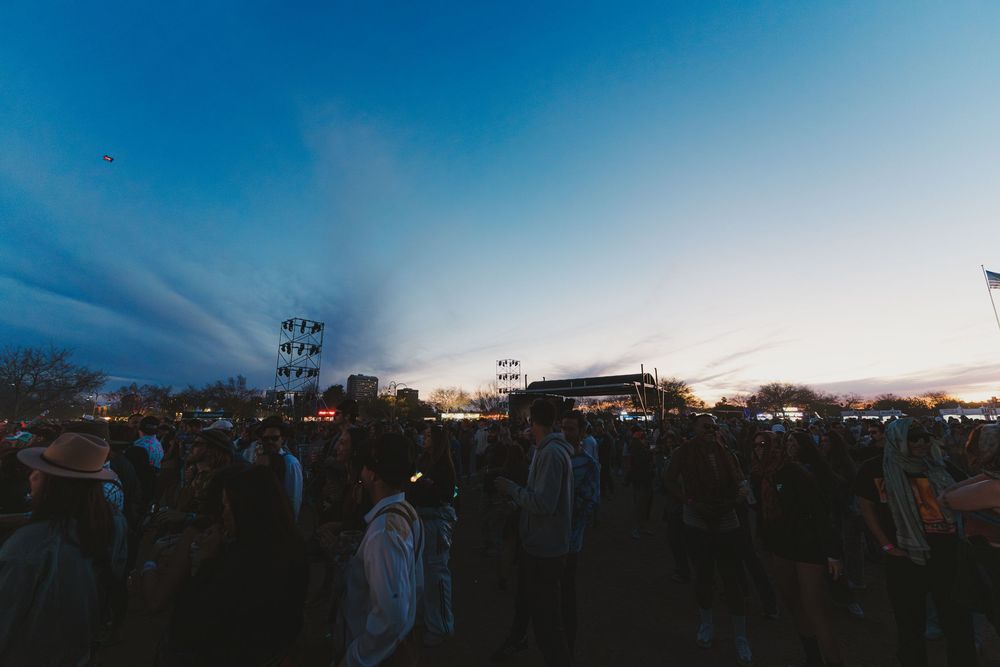 A panoramic view of a sunset sky with stadium lights and buildings silhouetted against the colorful horizon.