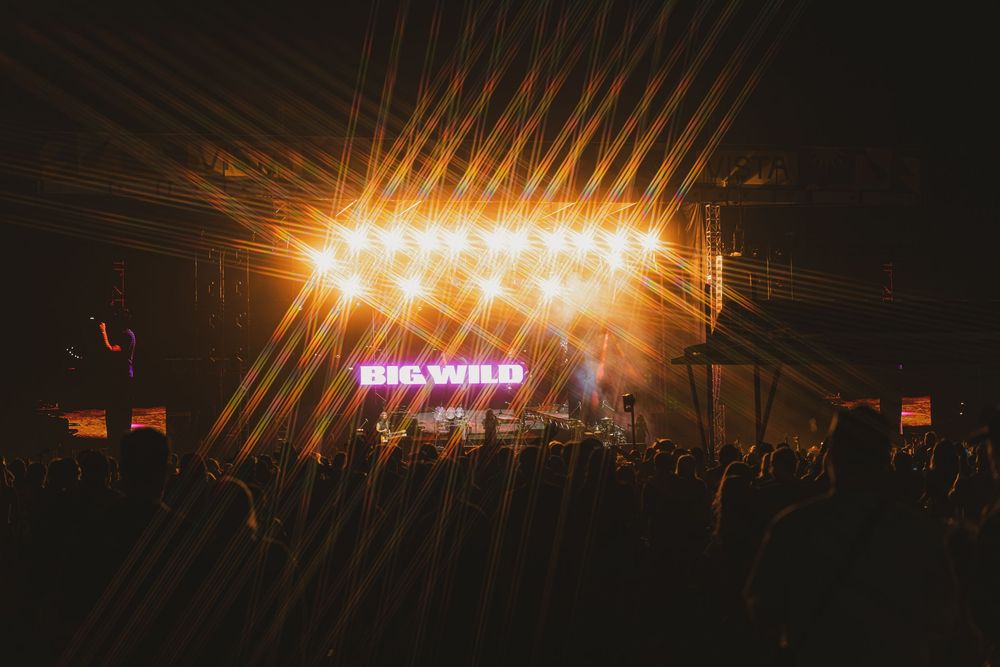 Concert stage lights shine brightly through a dark venue creating dramatic beams of orange and yellow light.