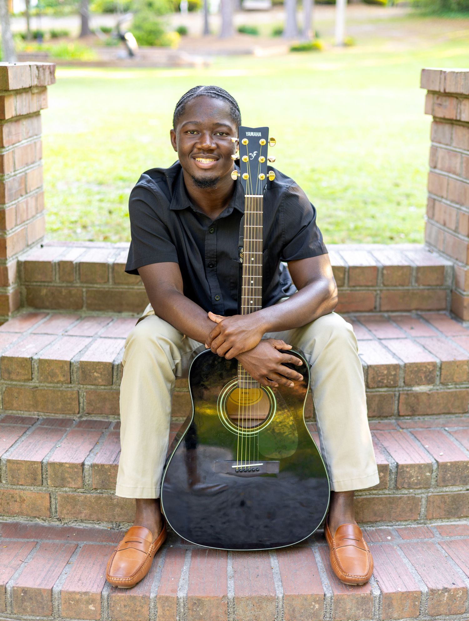 A musician in a black shirt sits on brick steps with an acoustic guitar in four similar poses.