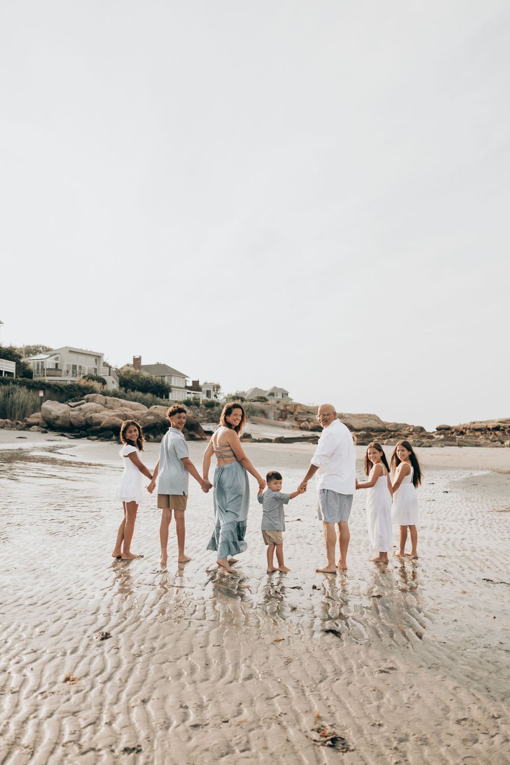 A group wearing coordinated light colored outfits walks together on a sandy beach at sunset.