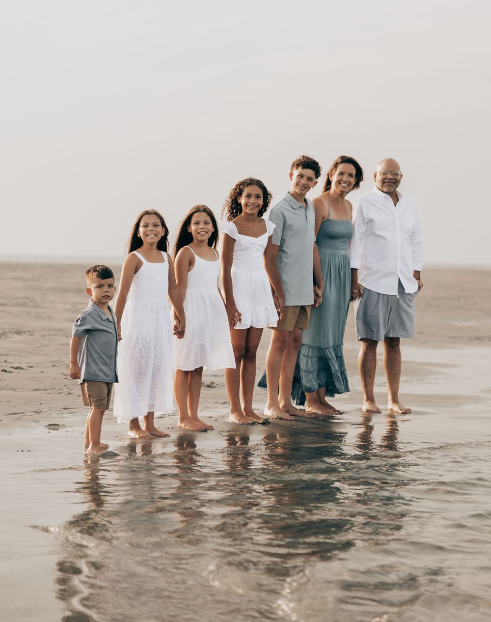 People stand in shallow ocean water along the shoreline wearing coordinated blue and white outfits.