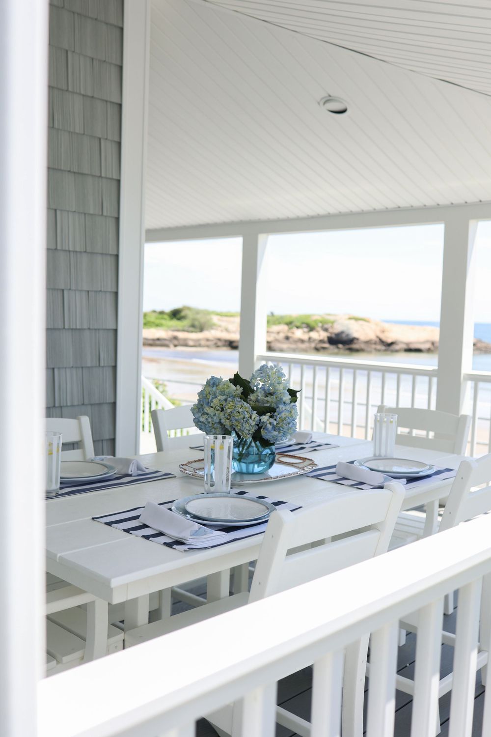 Coastal dining table set with blue and white decor on a bright waterfront porch.