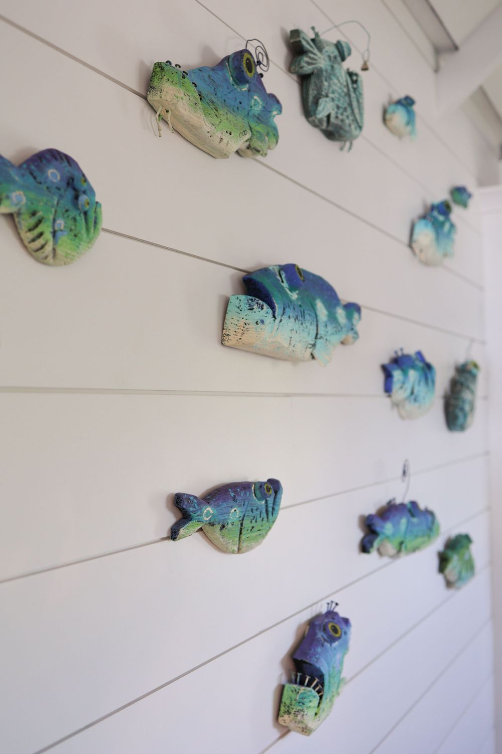 Colorful ceramic fish decorations mounted in a pattern on a white shiplap wall.