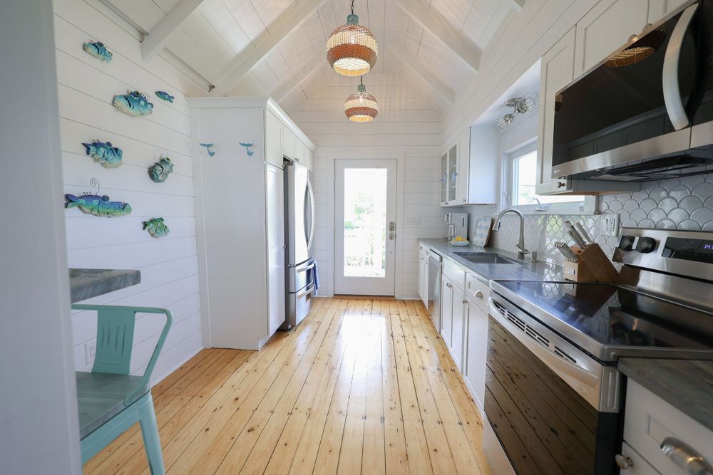 Bright coastal kitchen with wood floors and turquoise fish decor on white walls.