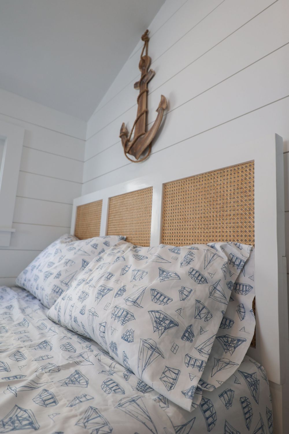 Nautical bedroom with wooden anchor decor and blue sailboat patterned bedding.