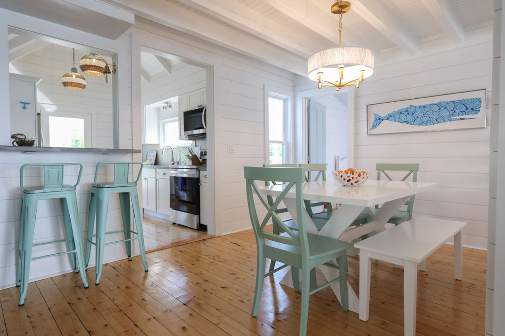 Bright dining area with mint green chairs and white shiplap walls in beach house style.