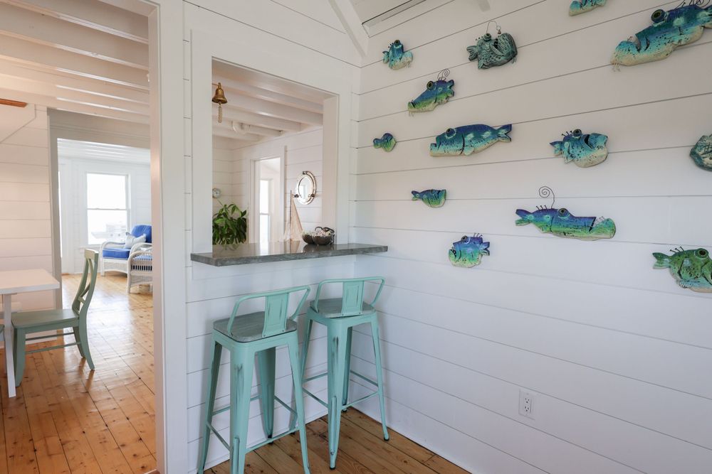 Coastal kitchen bar with mint stools and decorative blue fish mounted on white walls.