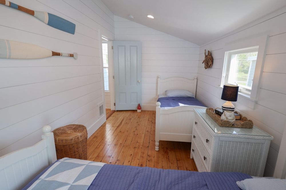 Bright beach bedroom with white shiplap walls, hardwood floors and blue accents.