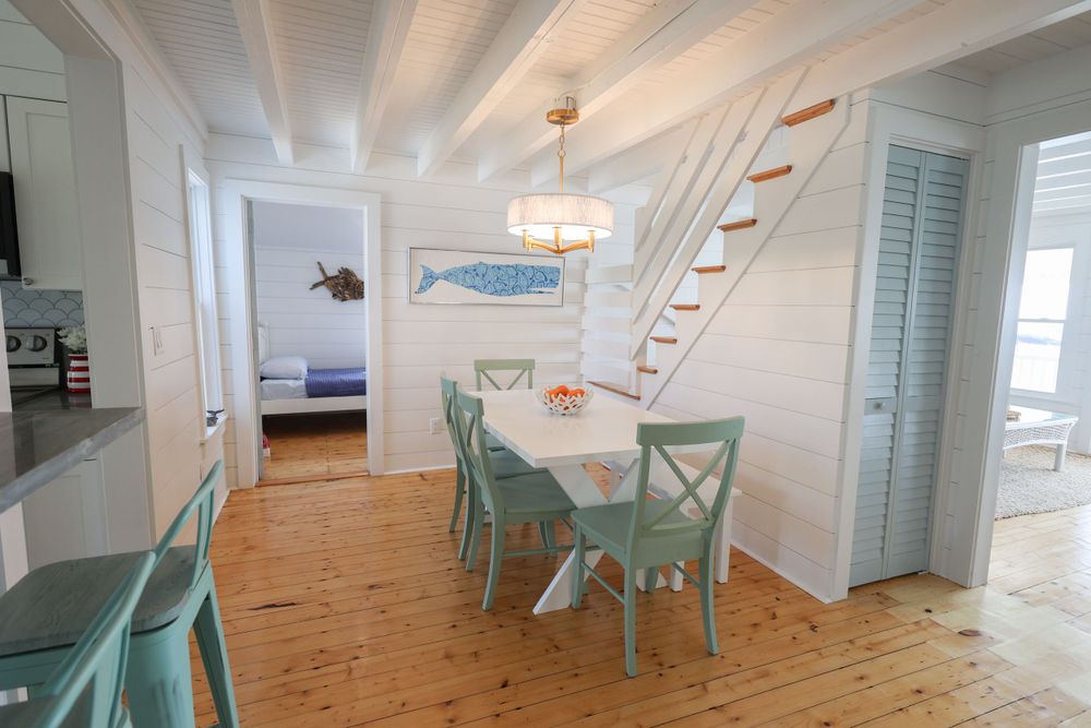 Coastal dining area with mint green chairs and a wooden staircase leading upstairs.