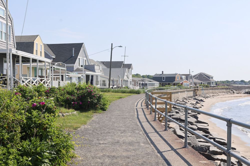 Beachfront pathway with benches overlooking the ocean and coastal homes.