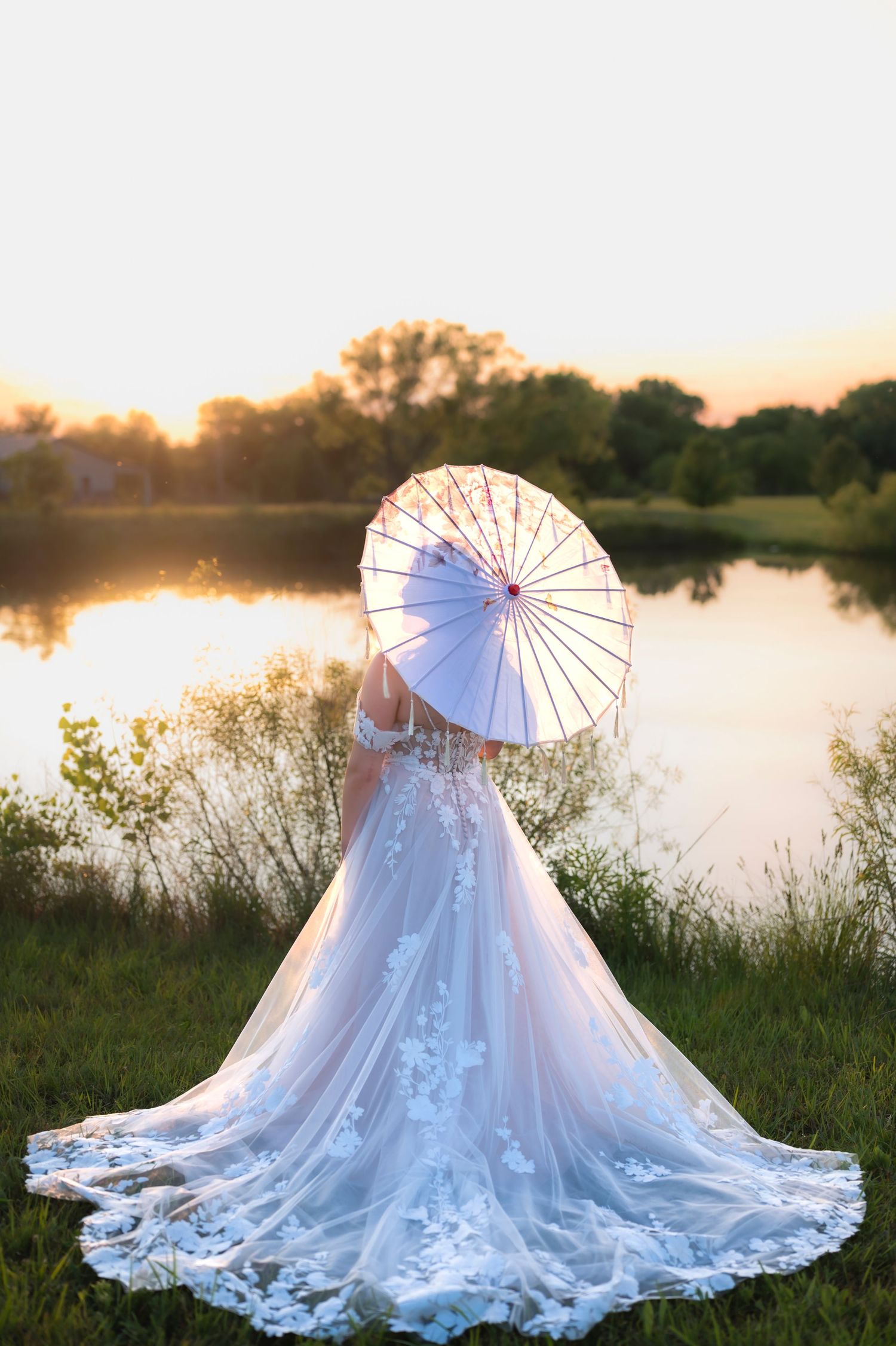 A bride and groom share an intimate moment by a riverbank in winter, with her white gown flowing in sepia tones.