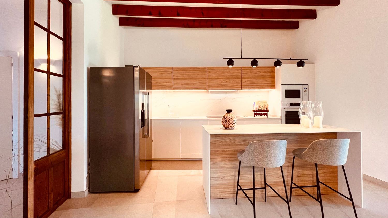 Modern kitchen interior with wooden cabinets, stainless steel appliances, and exposed ceiling beams in warm lighting.