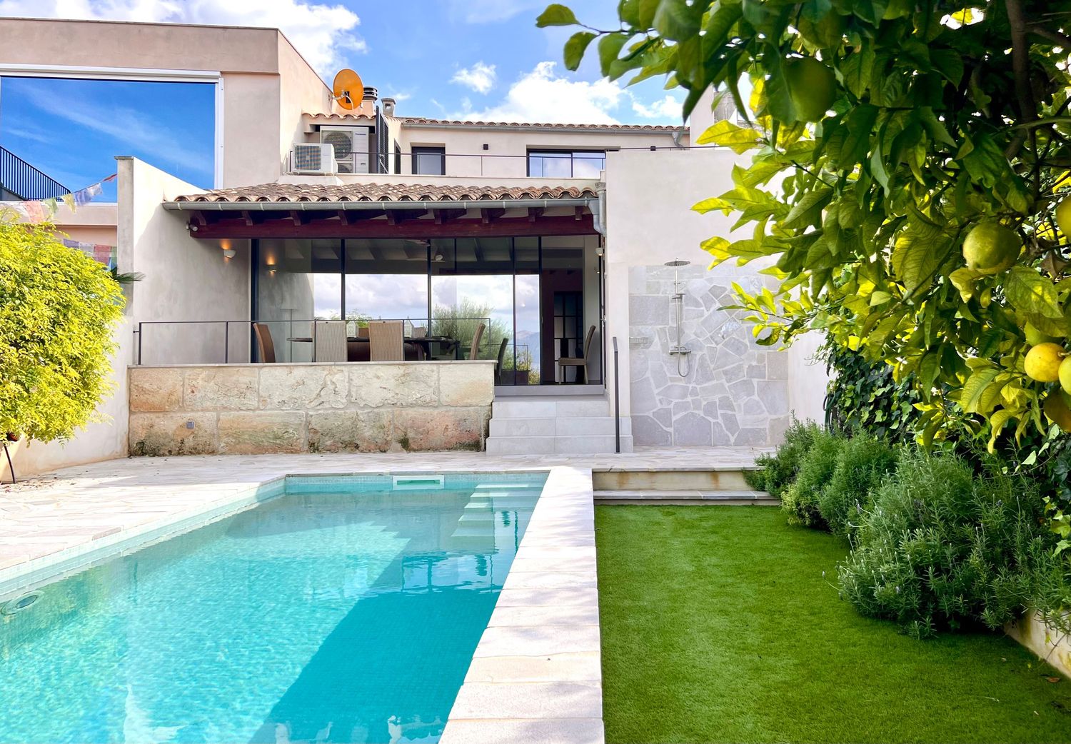 Modern luxury villa with concrete facade, wooden pergola, swimming pool and manicured lawn in sunny garden setting.
