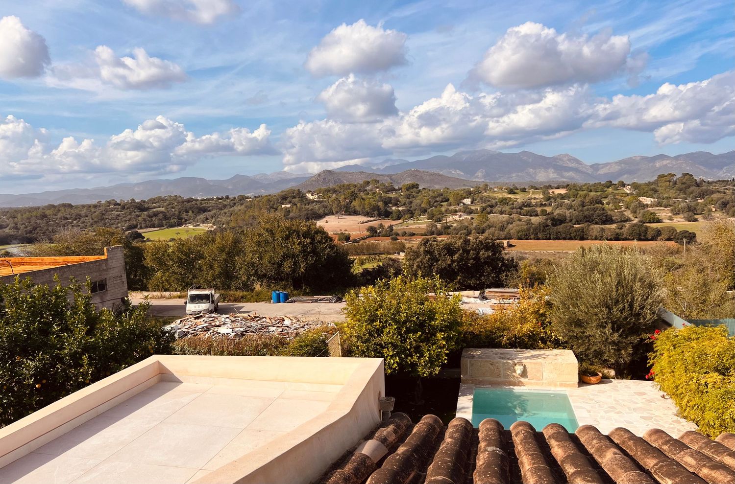 A panoramic view of a Mediterranean coastal landscape with mountains, buildings and lush vegetation under blue skies.