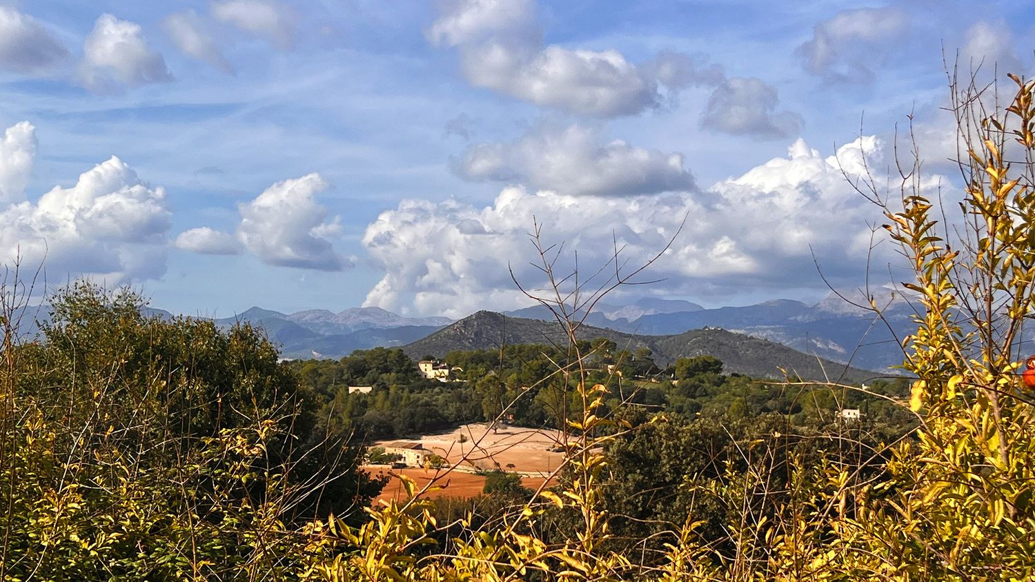 Scenic mountain landscape with golden autumn foliage under a blue sky with puffy white clouds.