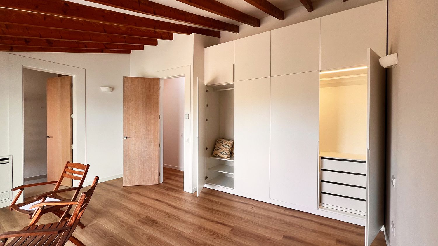 Modern bedroom with built-in white wardrobes, wooden floors, and exposed ceiling beams.