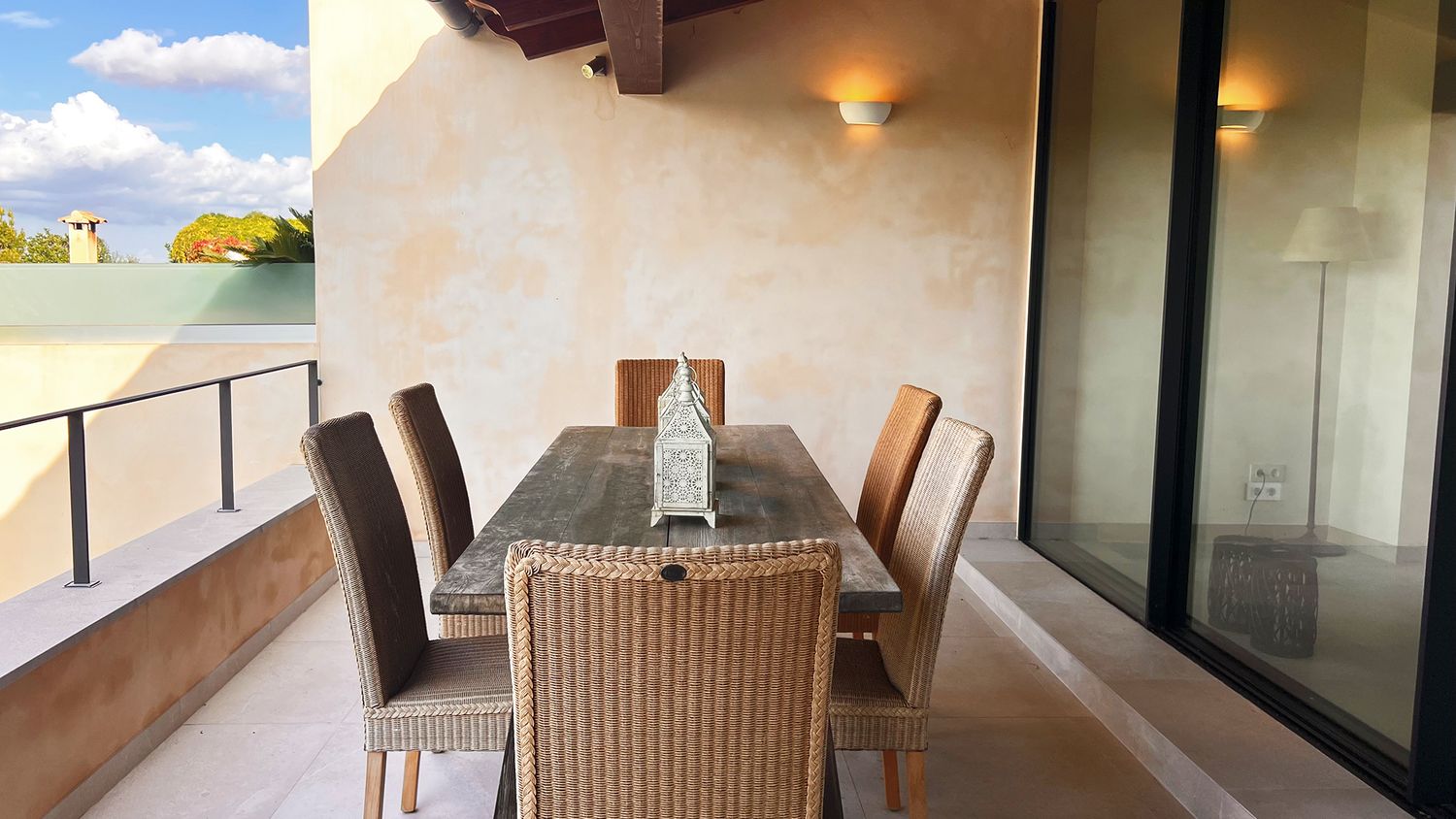 Covered outdoor dining area with wicker chairs and mountain view through glass doors.