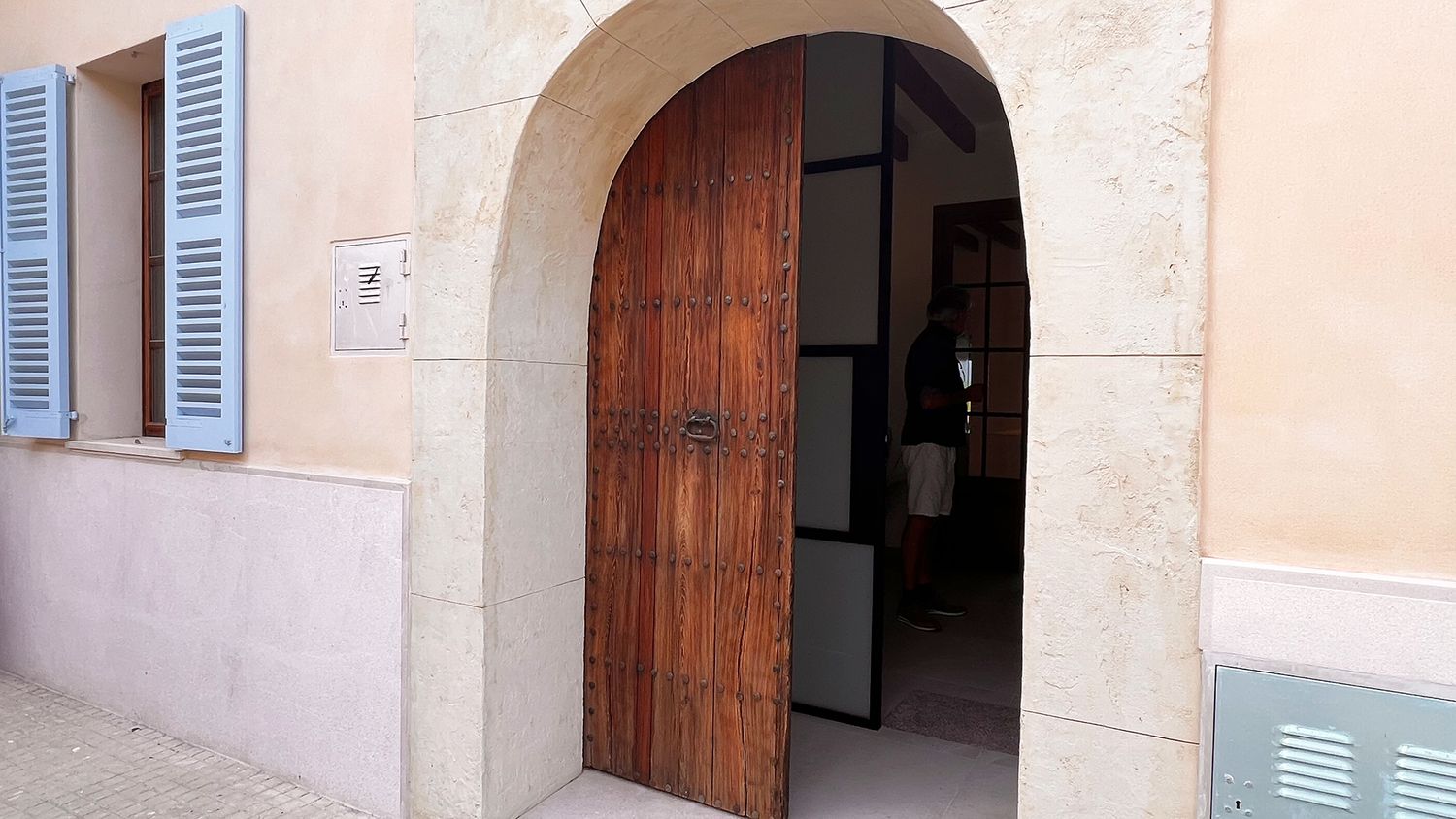 Traditional wooden arched doorway entrance with blue shutters on beige stucco wall.