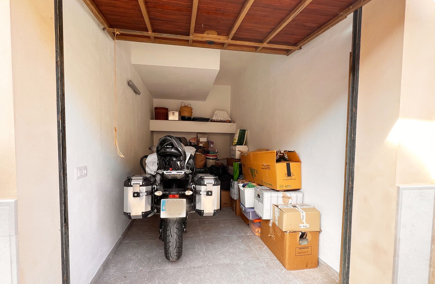 Garage storage space with motorcycle and cardboard boxes organized against white walls.