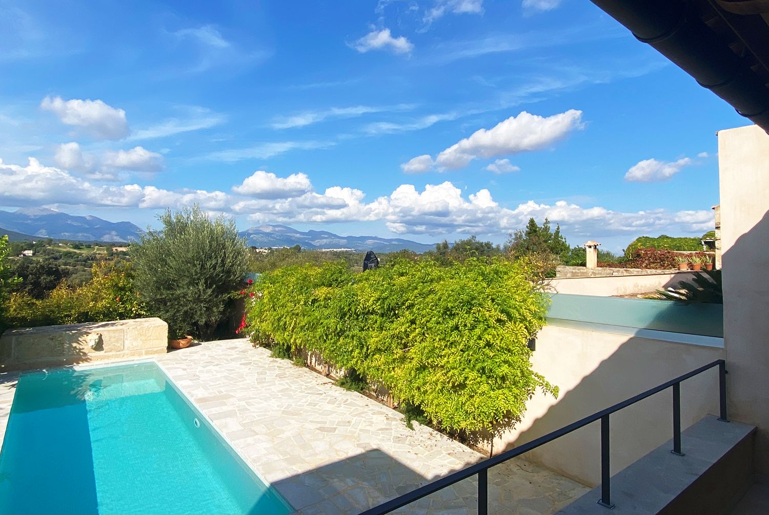 Modern villa terrace with infinity pool overlooking mountain landscape and blue sky.