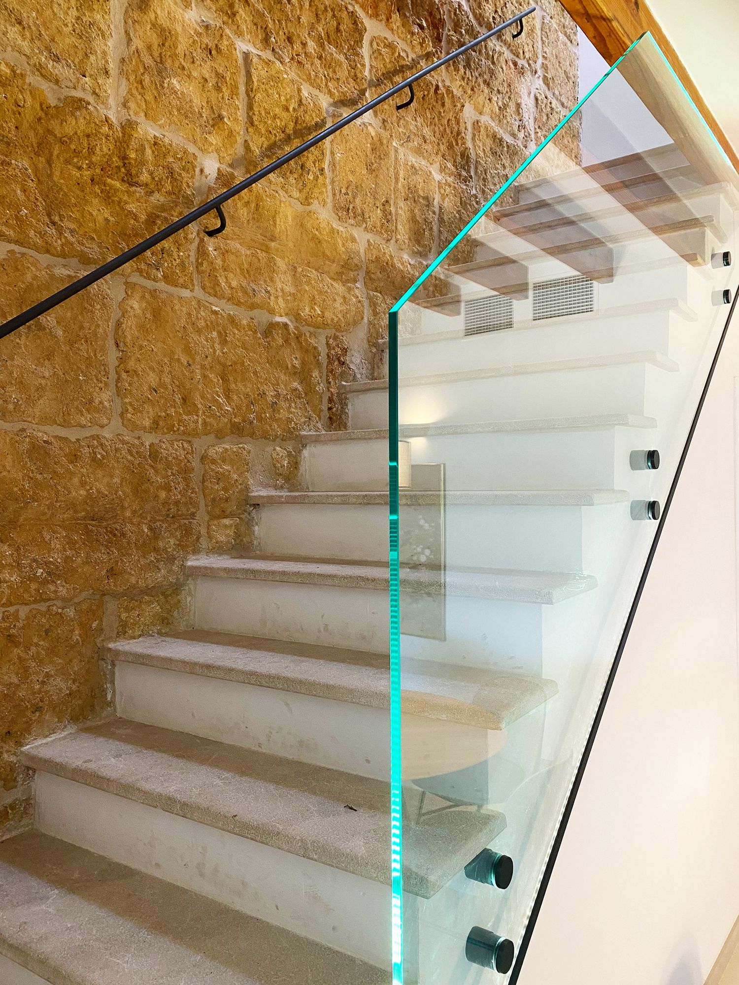 Modern staircase with glass balustrade, stone steps, and textured wall feature.