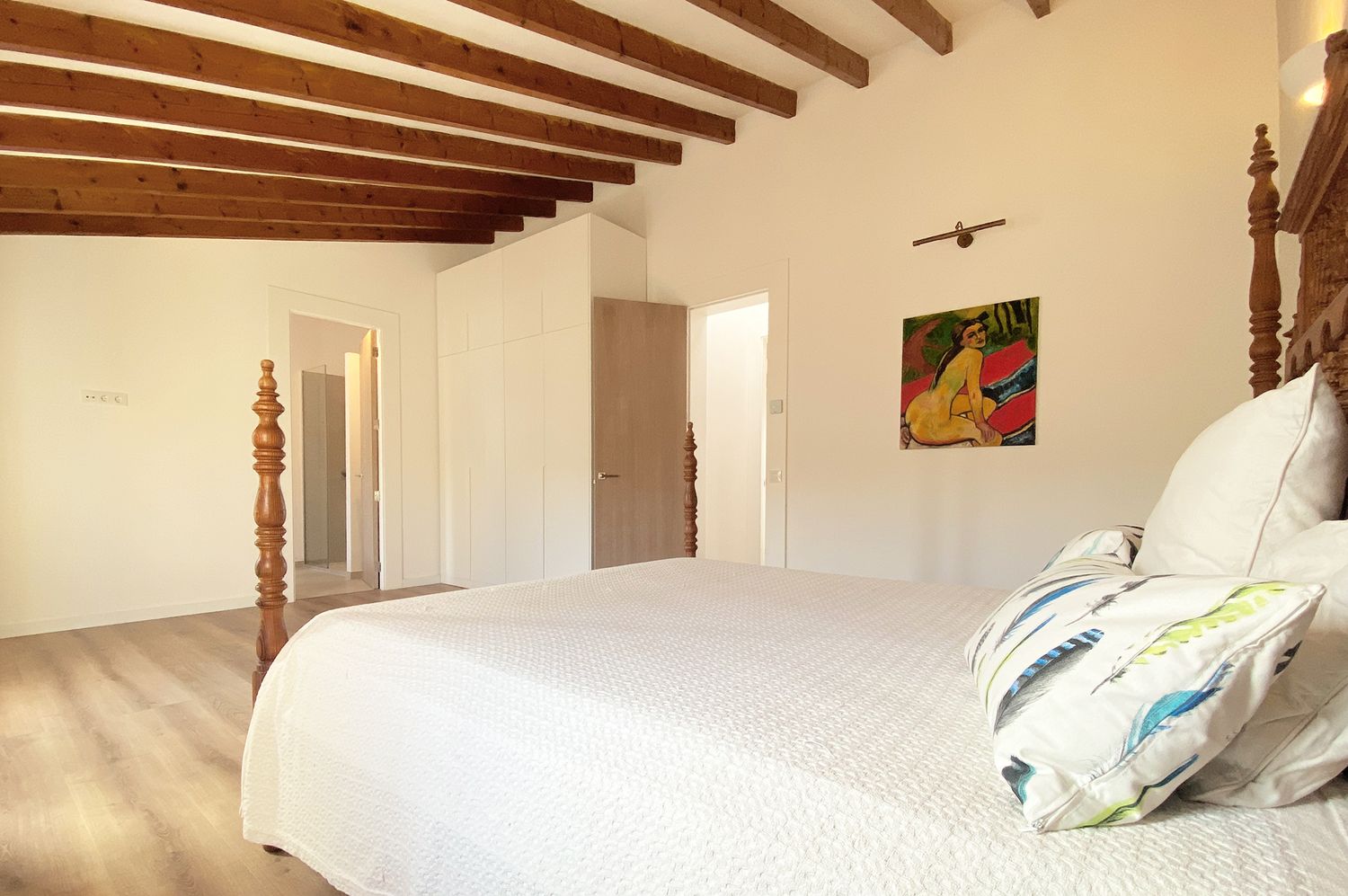 Bright bedroom with wooden beams and colorful wall art featuring white bedding and rustic decor.