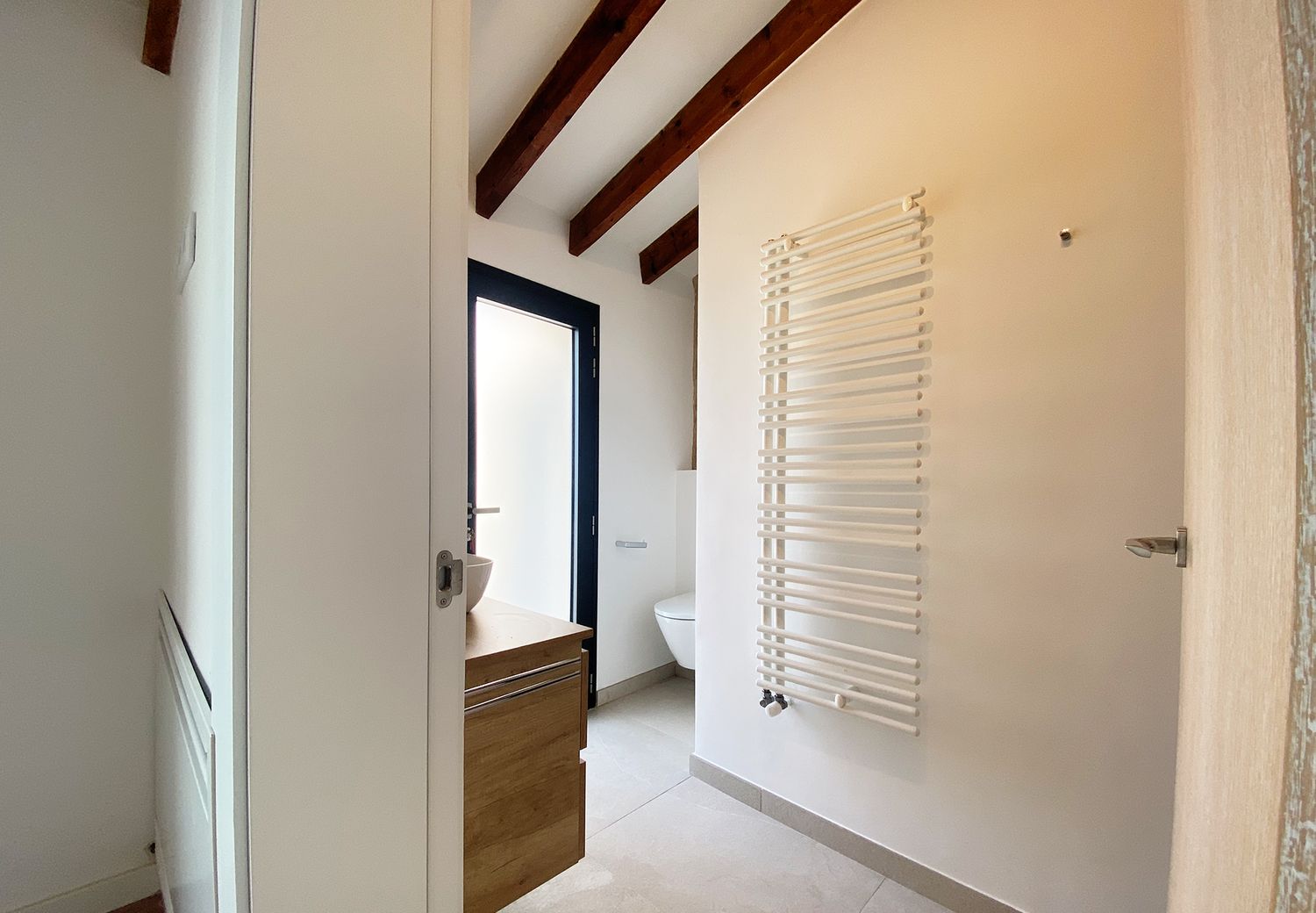 Modern white bathroom with wooden beams and heated towel rail.
