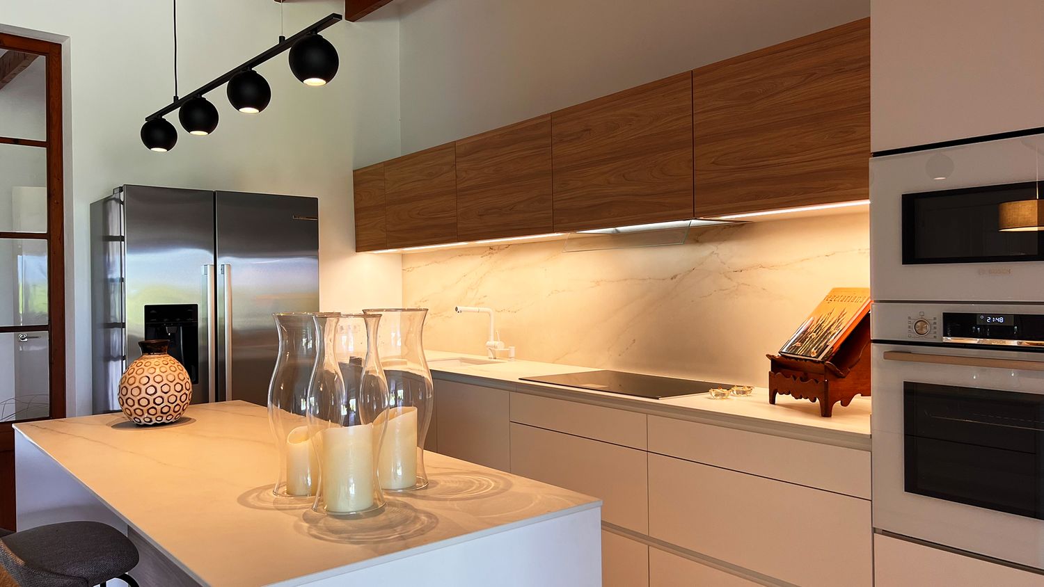 Modern kitchen interior with wood cabinets, track lighting, and a sleek white island under warm ambient lighting.